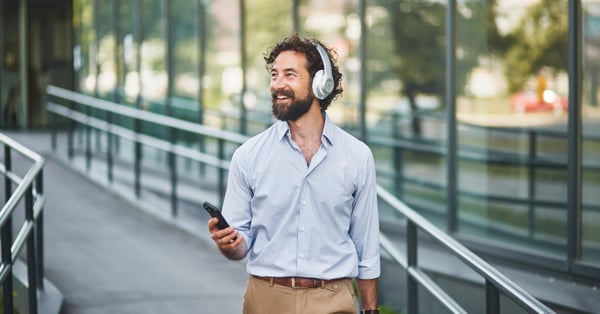 Businessman walking along the street listening to music and smiling