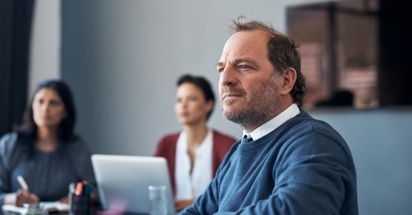 Male employee in blue jumper sat in a group meeting, looking attentively at the speaker off camera