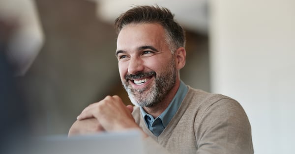 Man in beige jumper smiling across the table at unseen colleagues