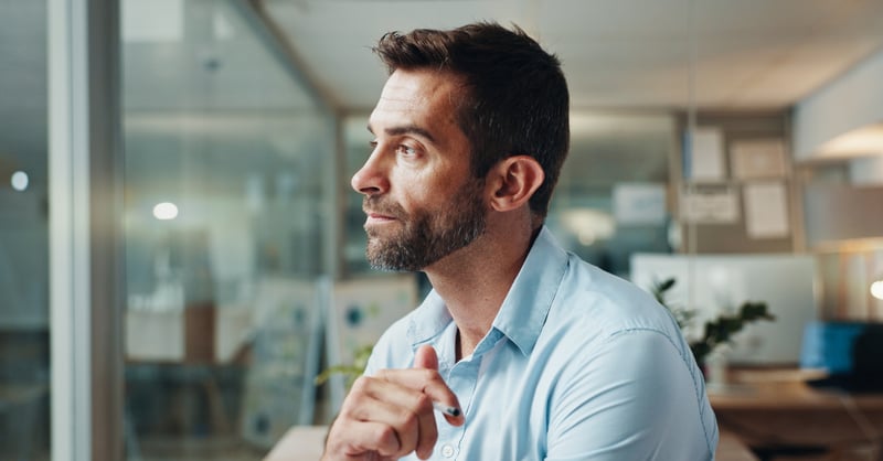 Business man in pale blue shirt looking pensively out of a window