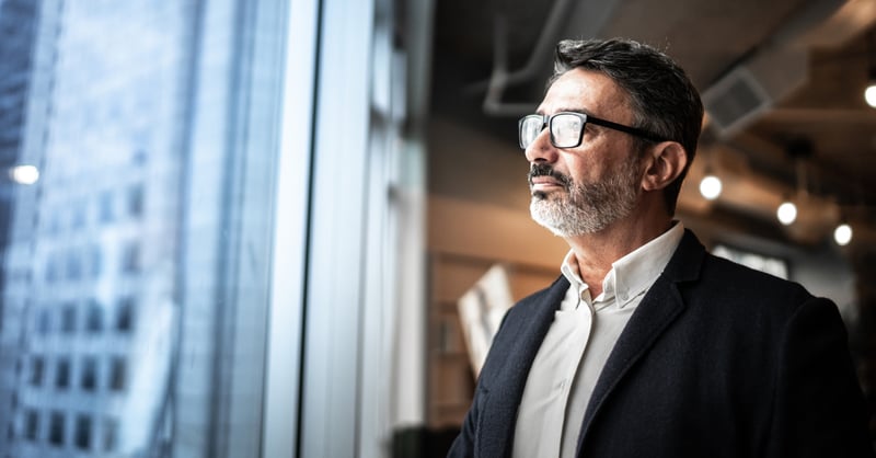 Senior business man in a white shirt and black blazer looking out the window