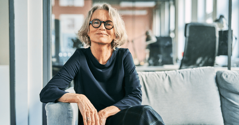 Portrait of a confident senior businesswoman sitting on a sofa in an office lobby, looking at the camera with a warm and professional smile